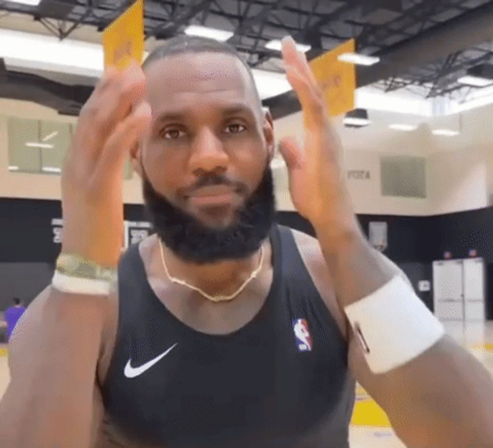 a man with a beard wearing a black nike tank top is standing in a gym .