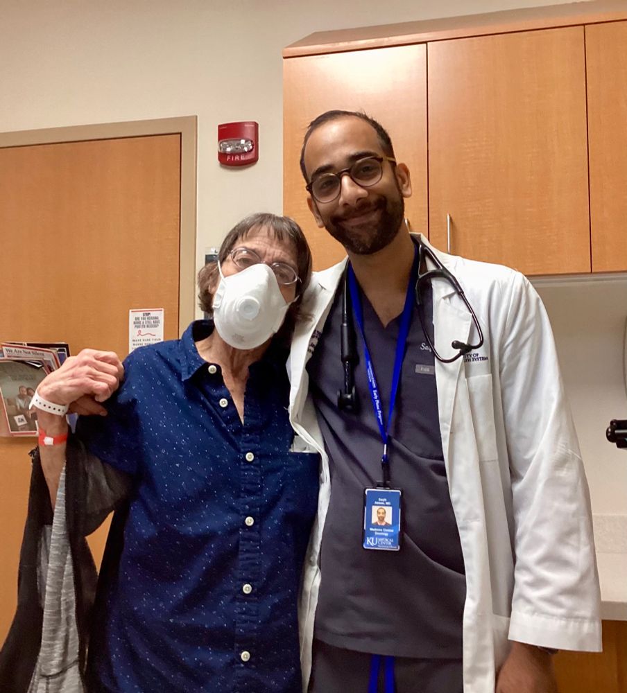 Dr. Abbasi in white lab coat and navy scrubs hugs star patient Liz in navy blue shirt with white buttons. Cancer fighting journey October 2024