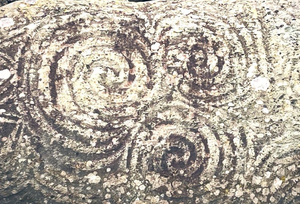 A photograph of a rock with a pecked engraving of three intersecting spirals.