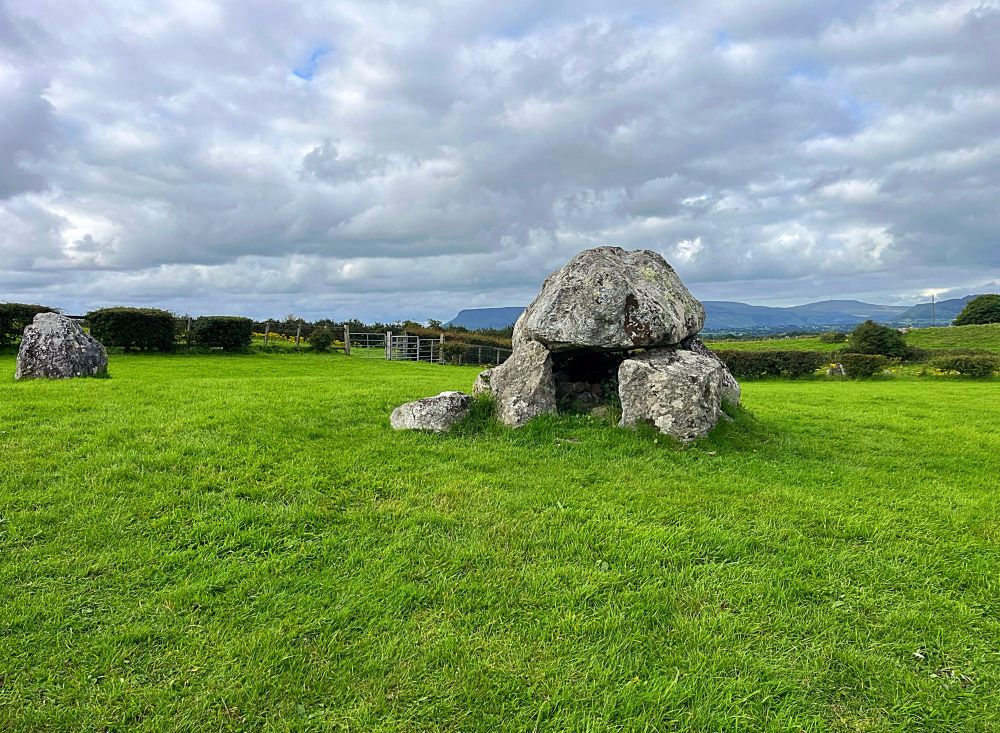 A photo of a grey mushroom-like dolmen on green short-cropped grass.