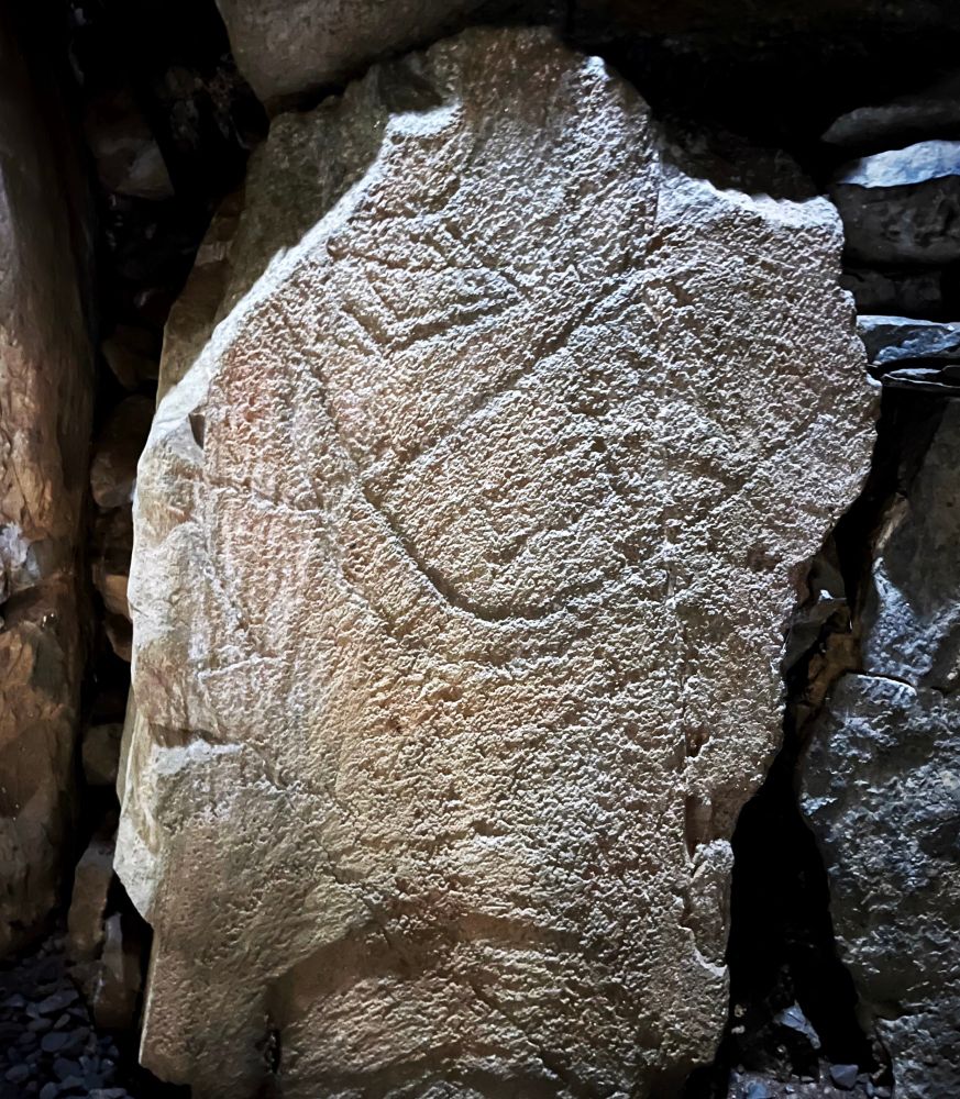A photo of a slab of rock with the engraving of a crude face and two lozenge-shaped eyes.