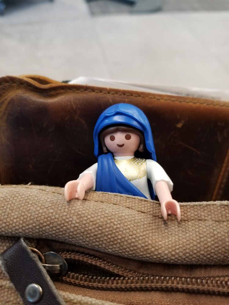 A Playmobil Hestia peeking out if a brown, canvas bag.