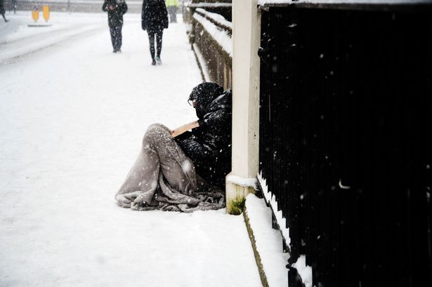 Rough sleeper sat on the pavement in the snow