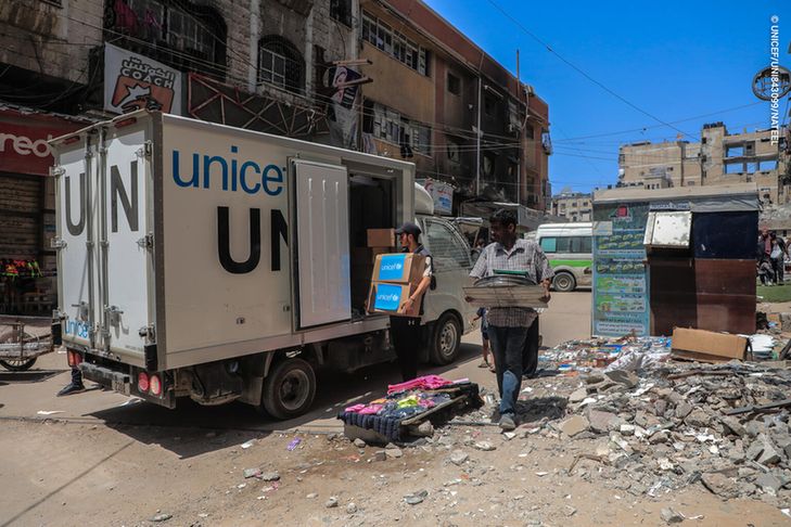 UNICEF staff unload a truck amid debris and damaged buildings