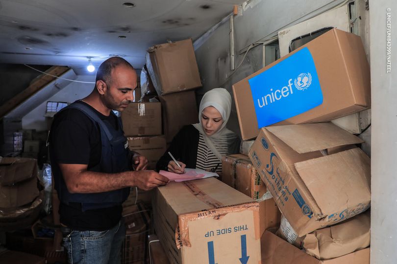 Two individuals review a list while standing near recently-arrived boxes of diapers