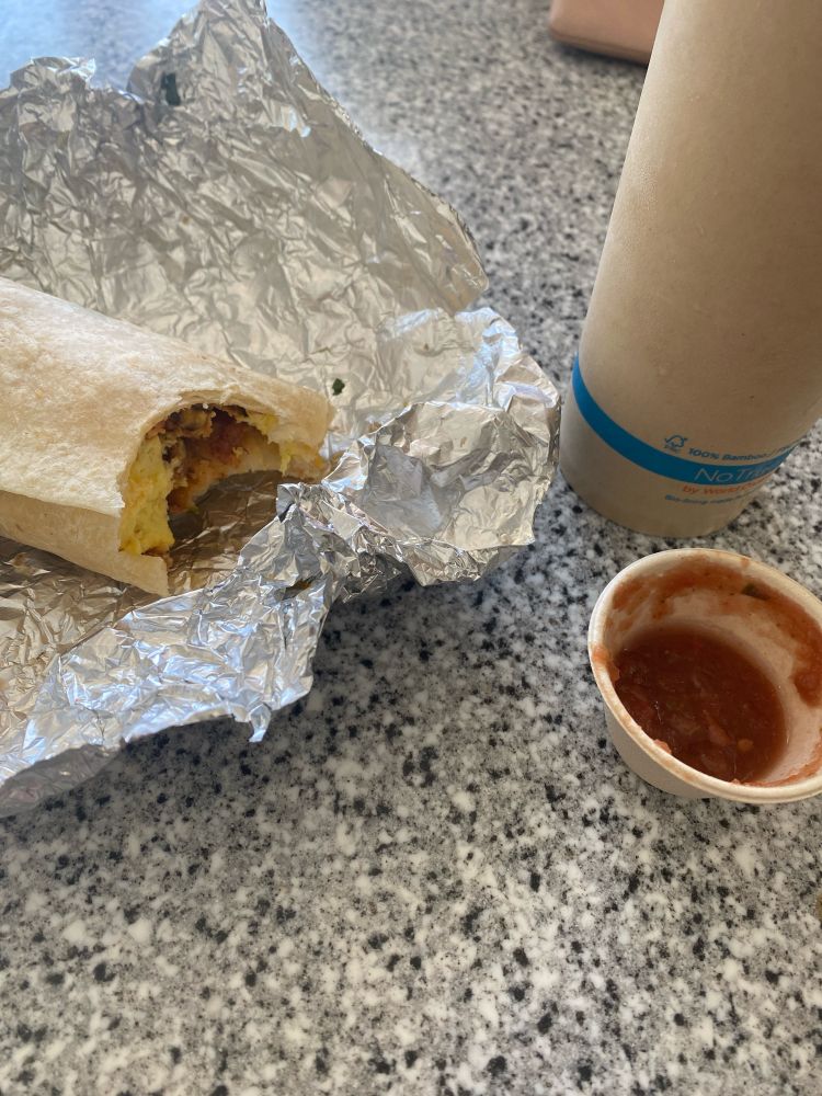 Half eaten burrito with salsa and coffy.