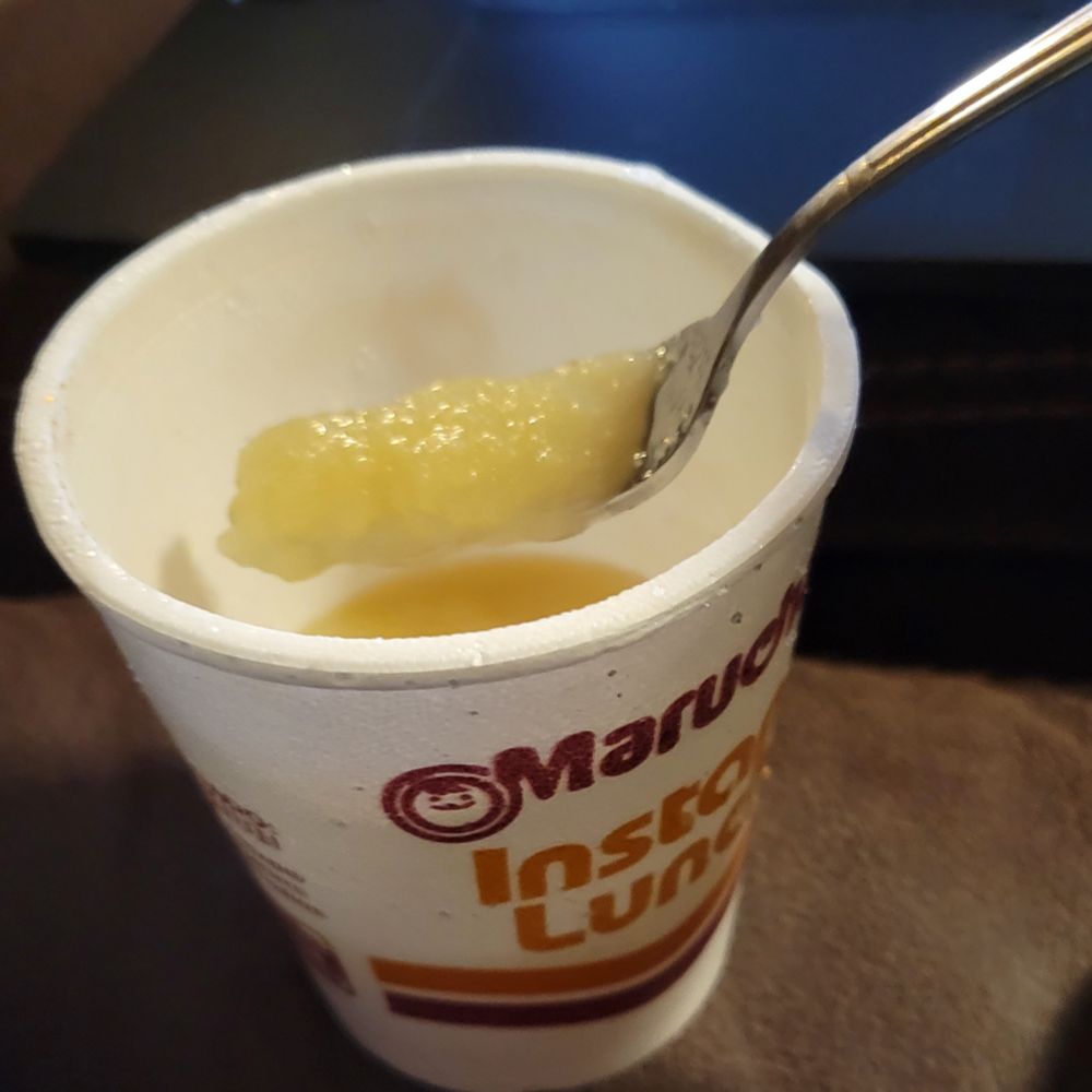 a fork spoons some applesauce out of an instant ramen cup