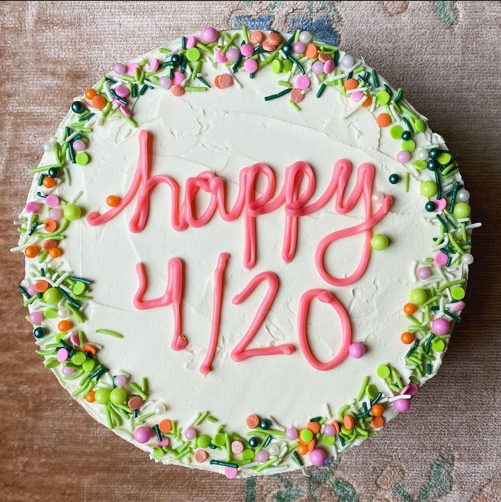A photo of a white cake with green and orange and pink sprinkles, and pink frosting lettering that says “happy 4/20”