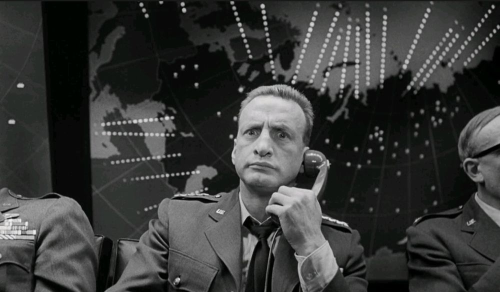 George C Scott in military uniform, on phone between other officers, face bugged out.