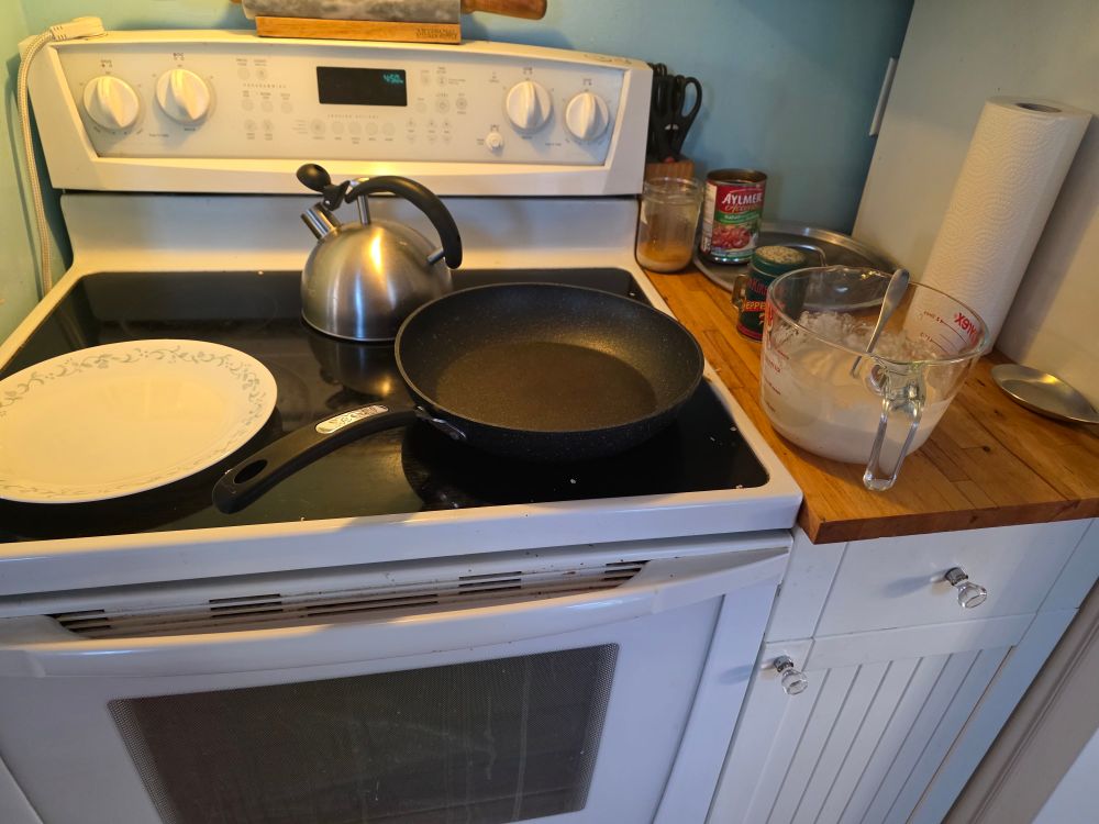 A plate and a pan on a stove with a large measuring cup of pancake batter