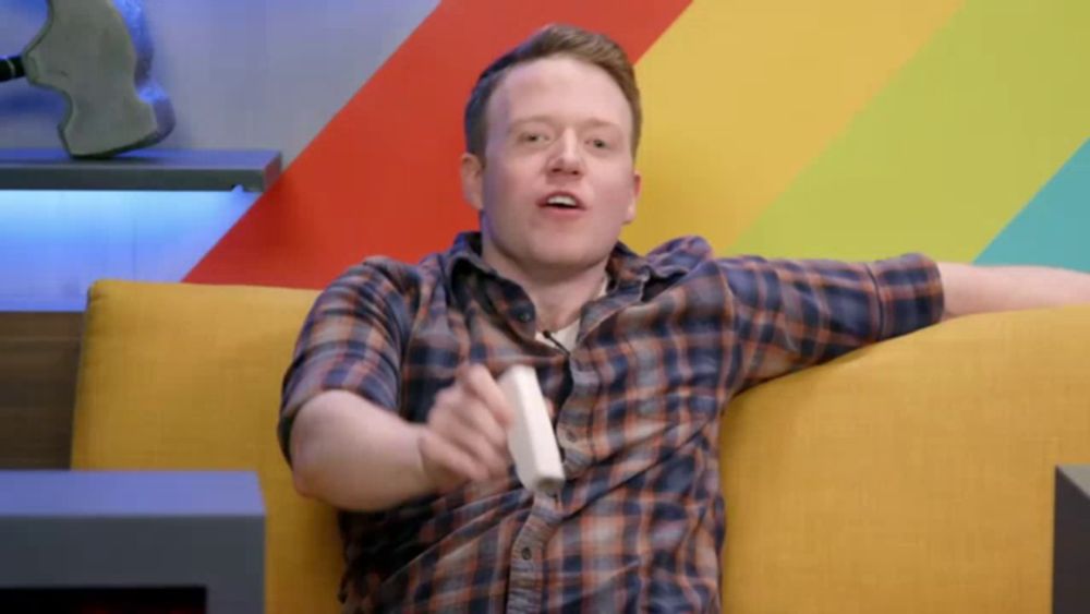 a man in a plaid shirt is sitting on a yellow couch holding a white controller