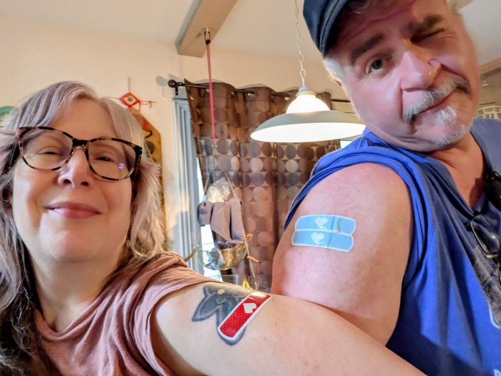 An awkward camera photo of fifty-something people flexing their booster-shot bandages because science is real