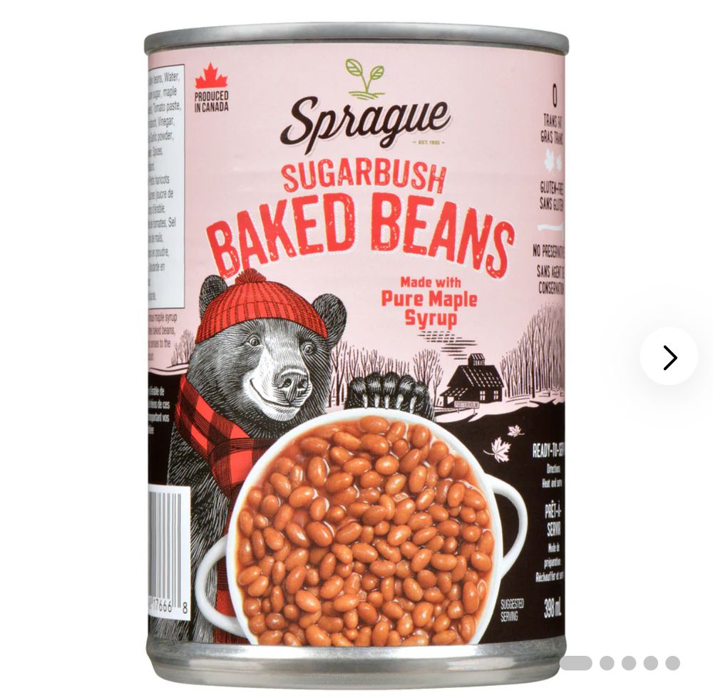 A picture of a can of baked beans from a company called Sprague. The label is pink with a cartoon a bear wearing a red hat and a red and black scarf. The print on the can is in red and says Sugarbush baked beans with pure maple syrup. and there is a picture of an actual bowl of beans