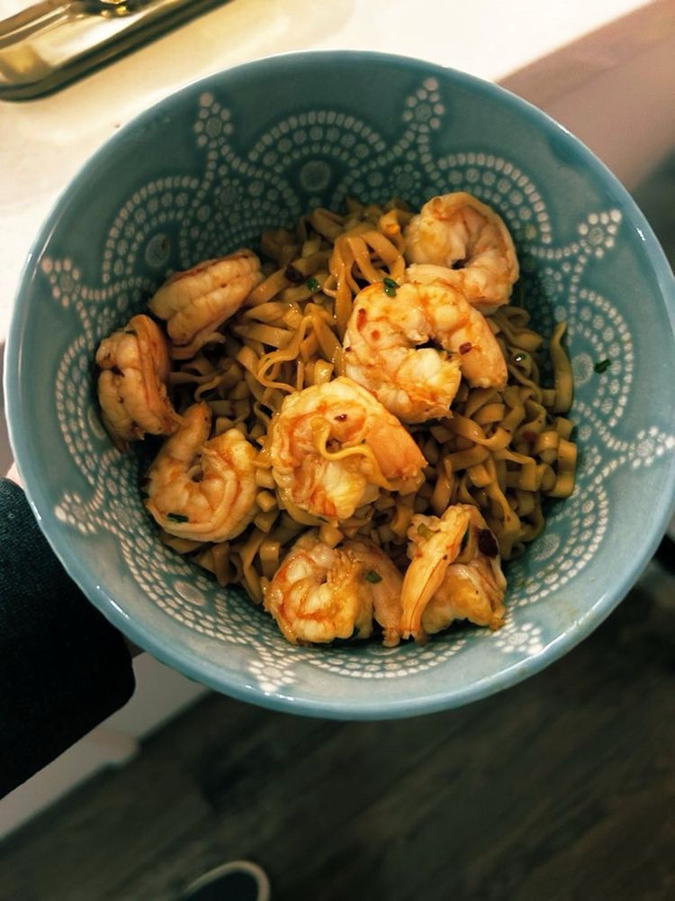 Blue patterned ceramic bowl filled with cooked shrimp and noodles. 