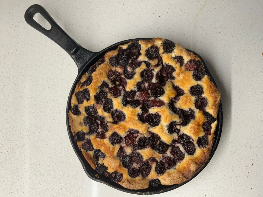 A cast-iron pan with a bake cake inside of it with cherries on top