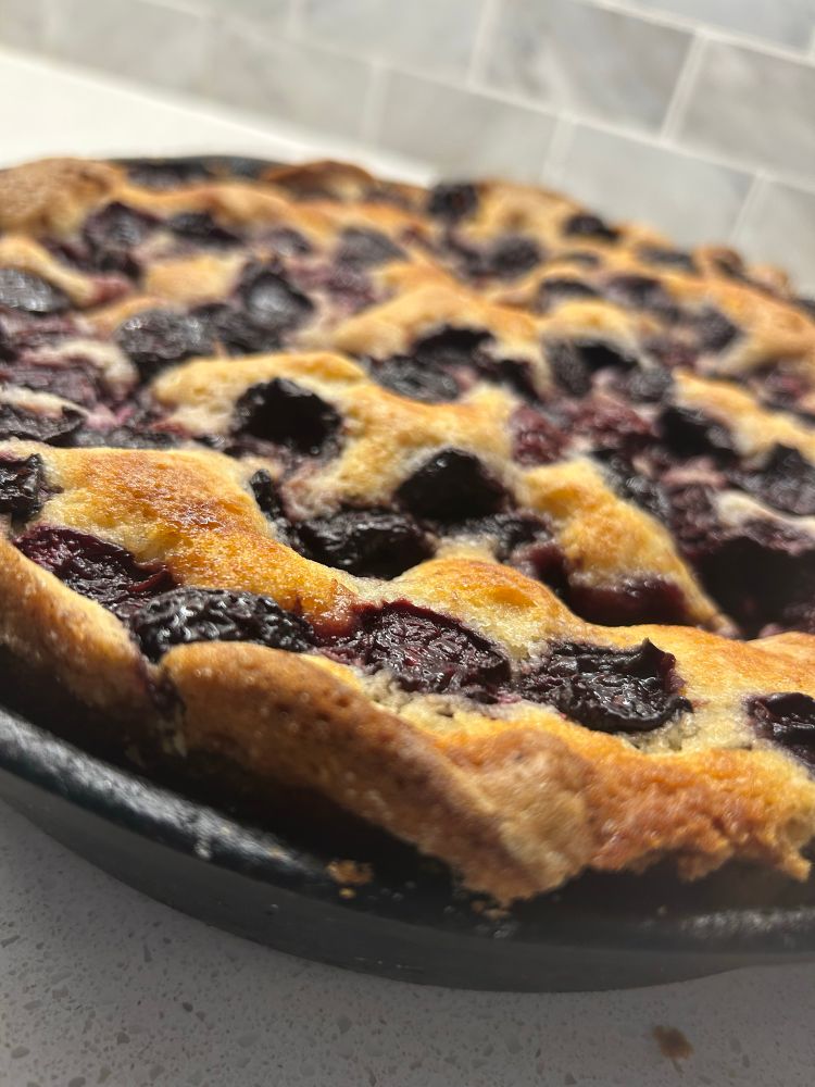 A close-up picture of a cake baked in a cast-iron pan that has stone fruit in it