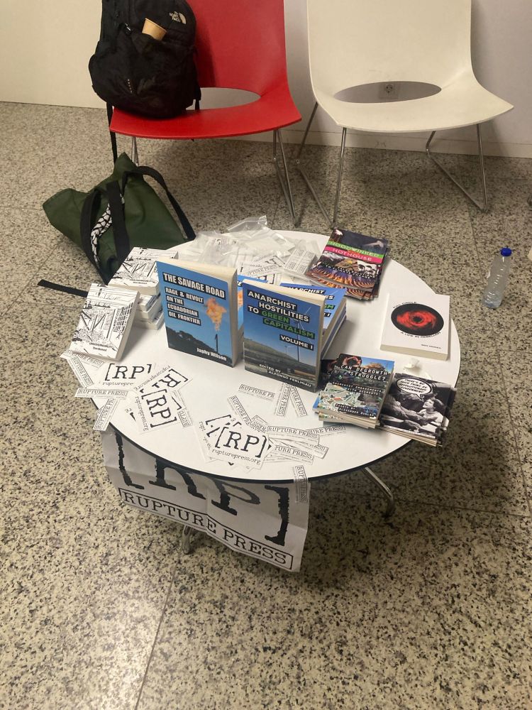 a small round table with a selection of Rupture Press books that are out + some other zines and Rupture Press stickers