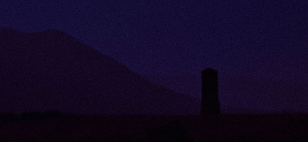 an image of the abyssal desert, whose vastness is incomprehensible. in the foreground stands a tall and foreboding obelisk, demanding the viewer's gaze. behind the obelisk lies great mountains, reaching up towards the starless sky.