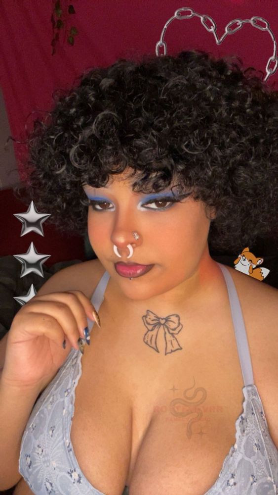 picture of theo, an ftm fem presenting fat person who’s Black, wearing a blue bra that’s holding his boobs up and blue eyeshadow to match, his hair is poofy and curly while he looks into the camera