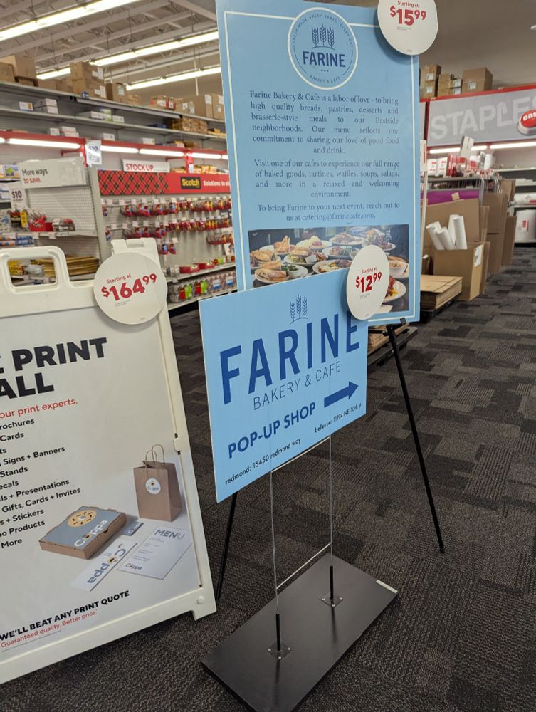 A bunch of advertisement signs, one that says FARINE bakery and café pop-up shop in dark blue lettering on a light blue background and round red on white signs that indicate the price of the sign.
