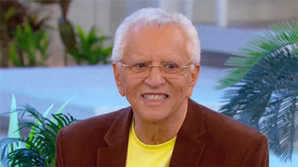 an older man wearing glasses and a yellow shirt smiles