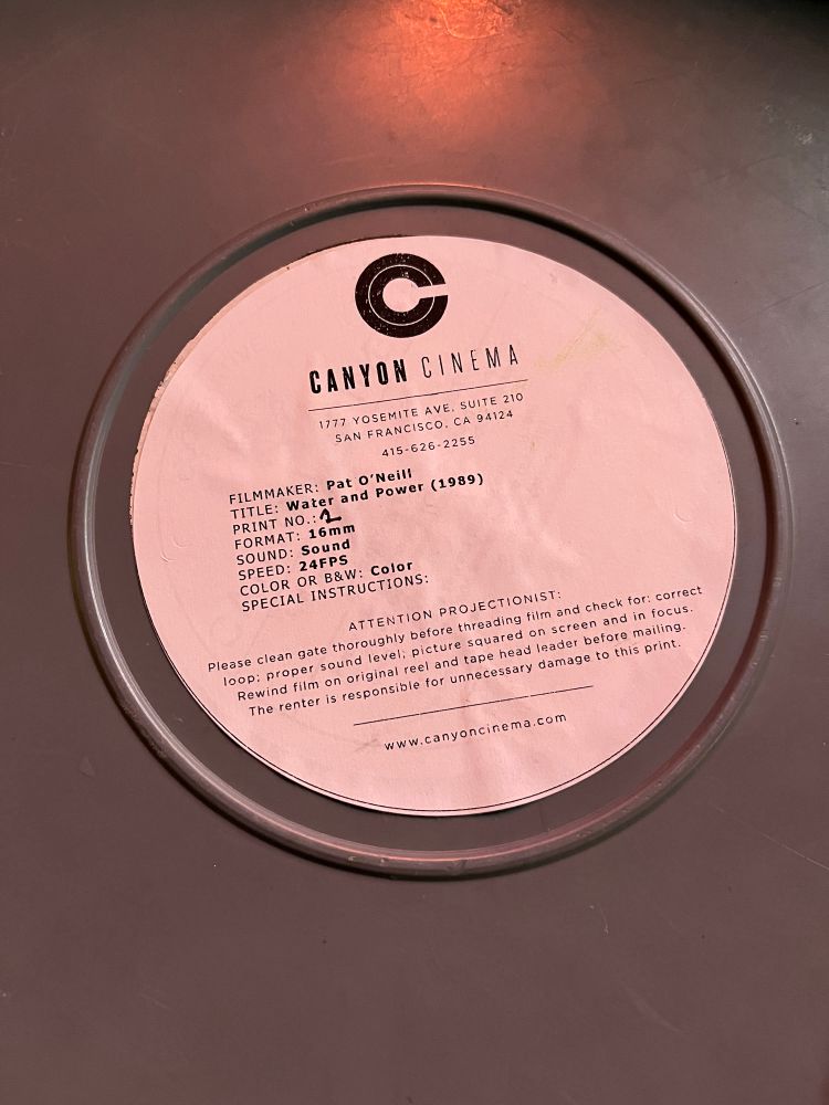 Image of a Canyon Cinema 16mm print of Pat O'Neill's Water and Power (1989) in its can with a label