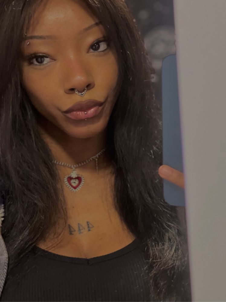 black girl taking a mirror selfie with heart necklace and 444 chest tattoo