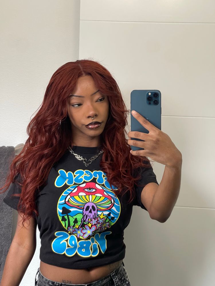 black girl with red hair wearing colorful mushroom shirt that says “fresh vibes“ in mirror selfie