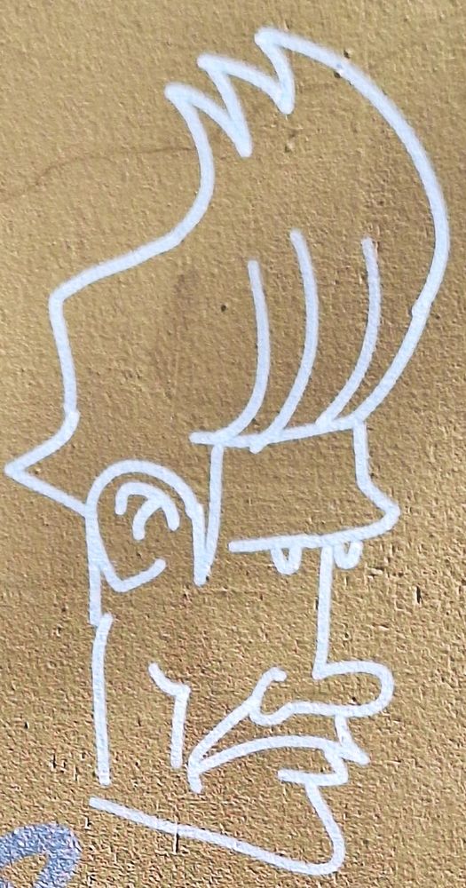 White line graffiti on a yellow-brownish wall, depicting a stern or grumpy looking man with a moustache and a high, wild hairdo