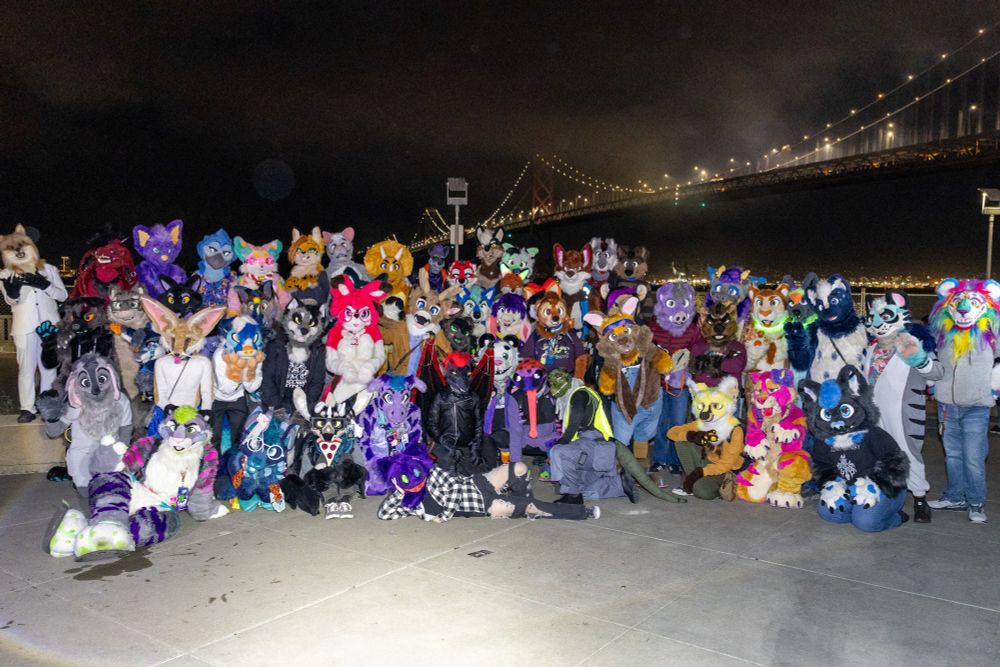 A group shot shows all ~54 fursuiters posed in front of the Bay Bridge.