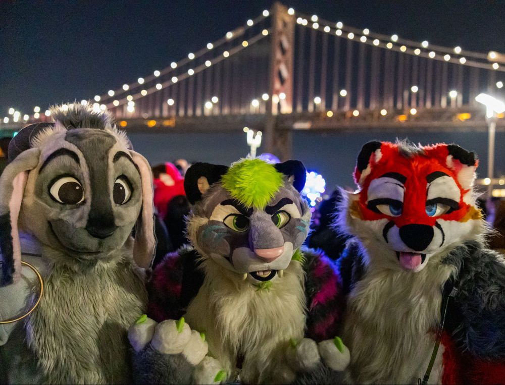 Jolly Goat (Hoofurs), Torq (Groggy), and Scout pose in front of the lit Bay Bridge in San Francisco on New Year's Eve 2024.