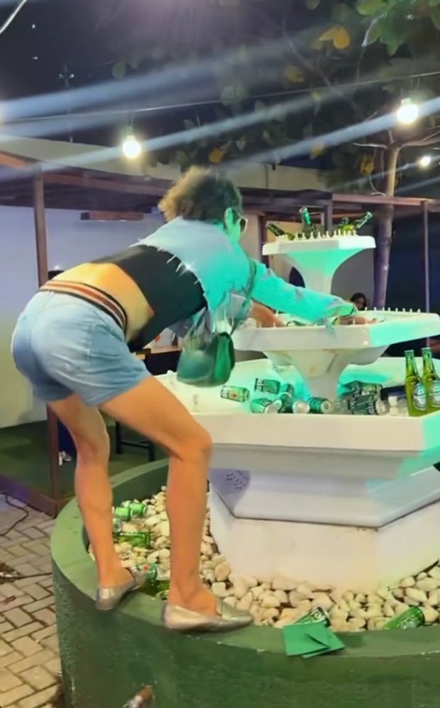 Uma pessoa agarrada numa fonte de água desligada mas com um monte de garrafa de cerveja 