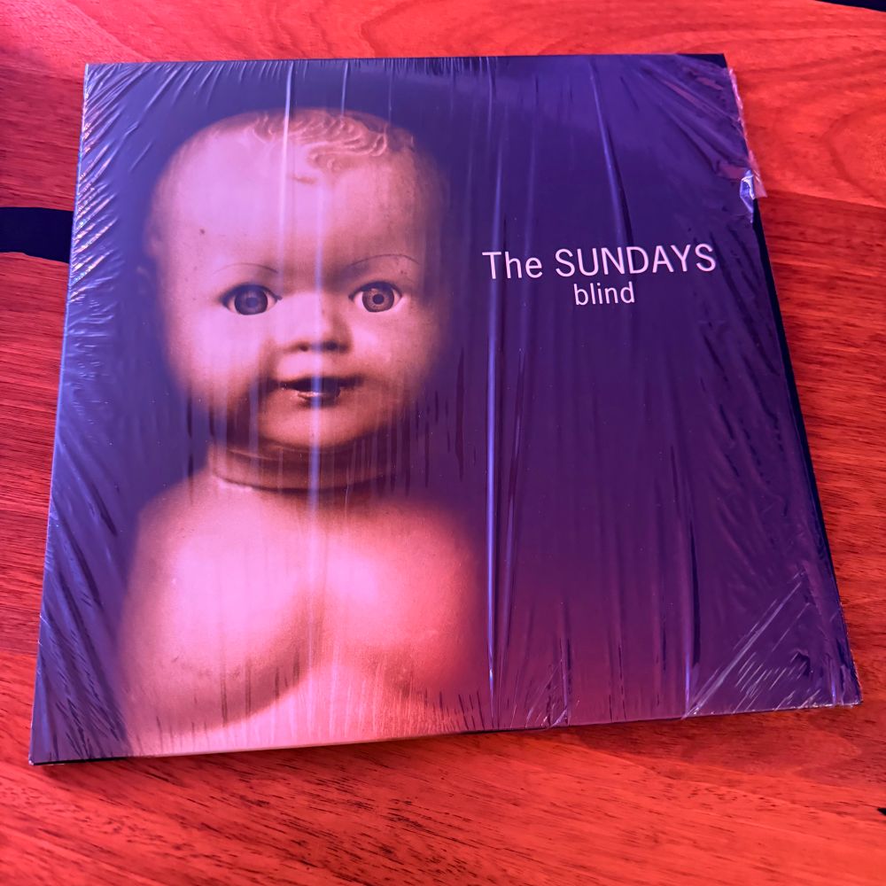 LP novo com o plástico da embalagem recém aberto do Blind, segundo álbum da banda The Sundays com uma boneca sem roupa numa capa preta. 