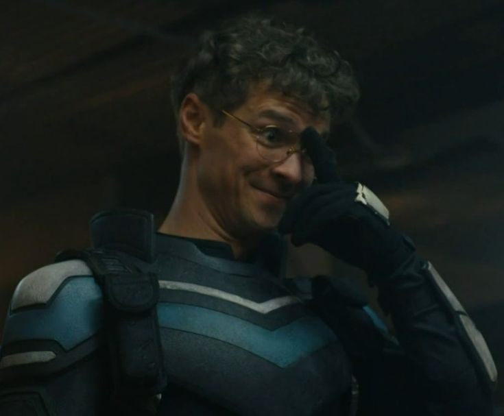 photo of adrian chase pushing his glasses up. he is in his vigilante suit sans mask, also looking quite cute