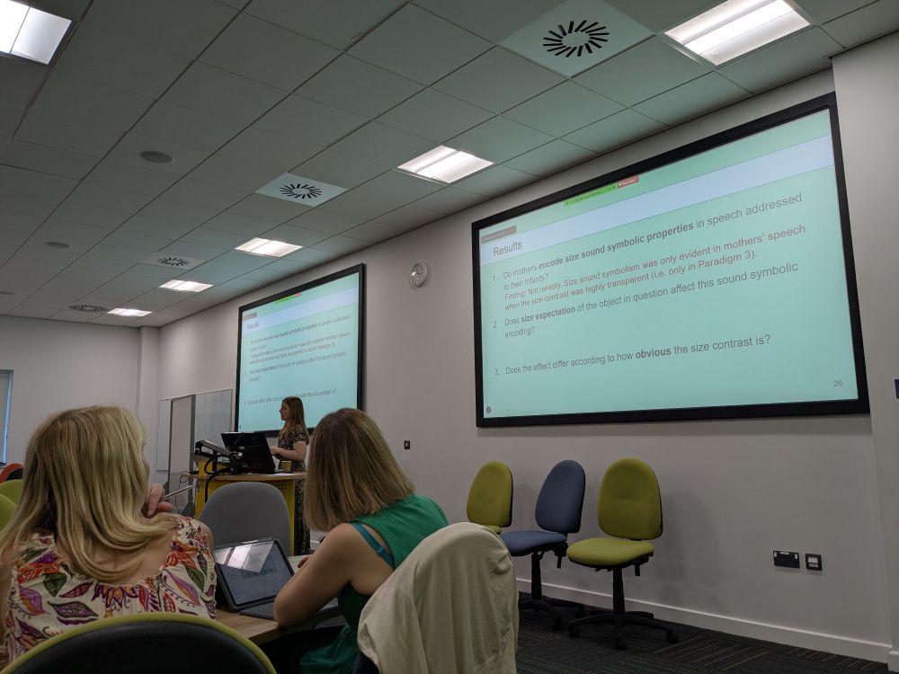 Catherine Laing giving the first talk - we can see Catherine beside a large screen with the talk slides on it, and some listening teachers in the foreground.