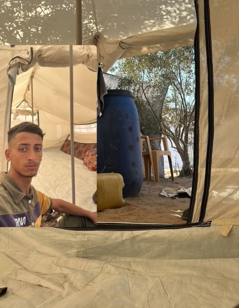 A young man in his tent, trees and water visible through the door. 