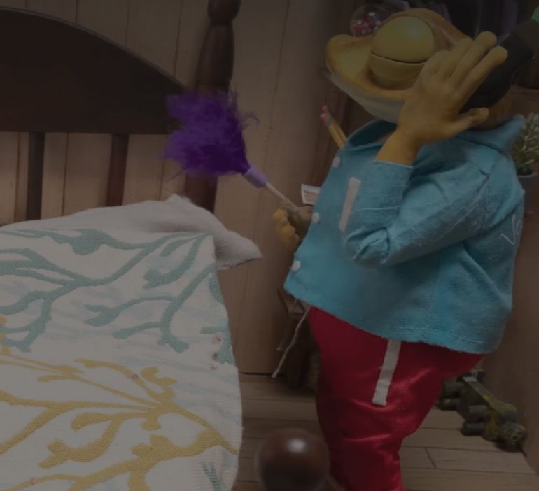 Animated anthropomorphic frog cleaning bedroom with purple feather duster while listening to music through headphones 