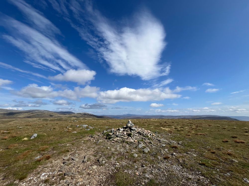 Summit cairn in the foreground with blue sky and cloud behind. 
