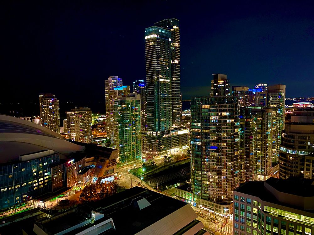 A photo of the City of Toronto, taken at night and from some height. Buildings and a portion of the Rogers Centre are illuminated by street and window lights. 