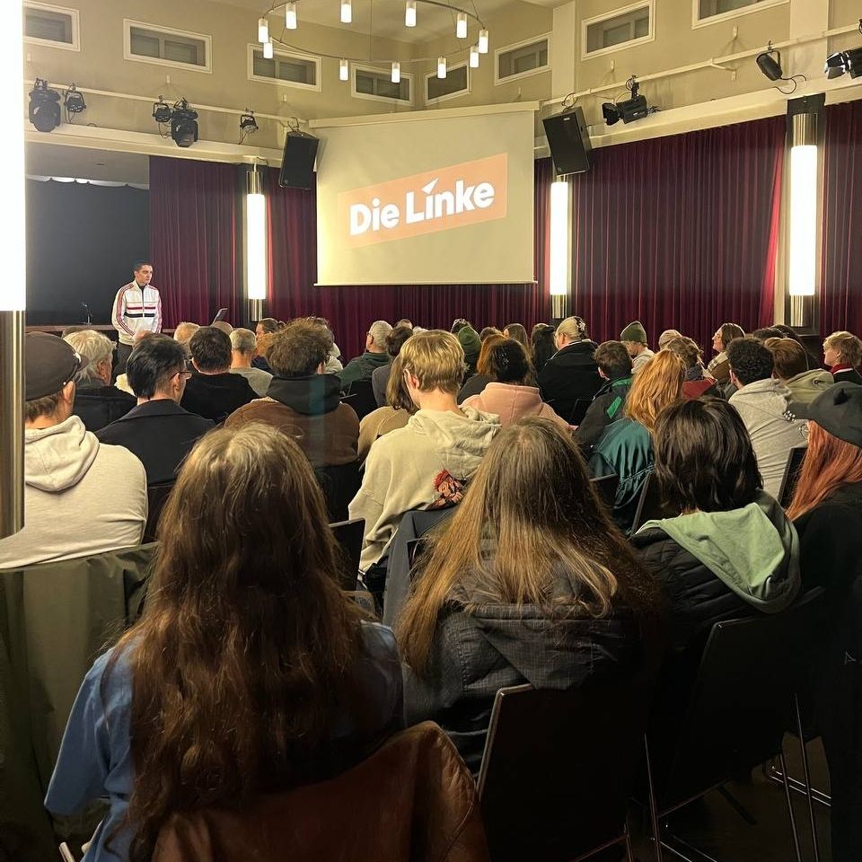 Saal voll gefüllt mit sitzenden Genoss:innen. Vorne stehe ich und moderiere das Neumitgliedertreffen Der Linken Bremen.