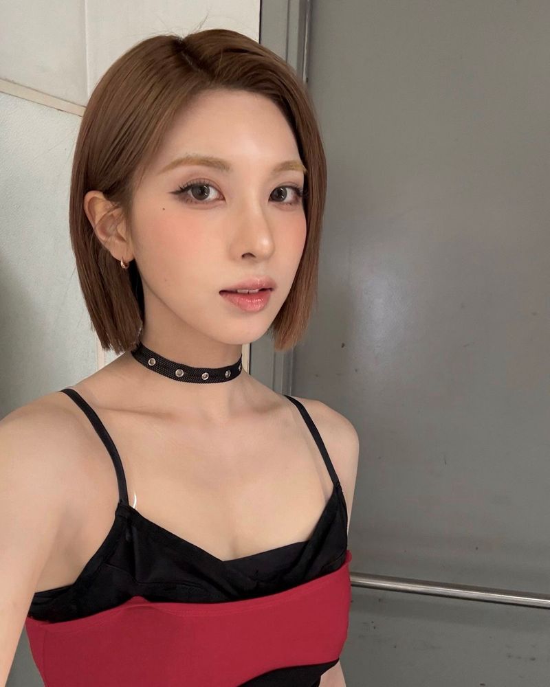 Selfie 2 of bae with a short light brown blunt bob wearing a black and red rank top and looking at an angle at the camera 