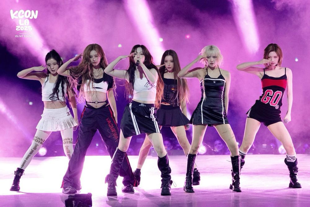Official photo of kpop group nmixx onstage at kcon L.A. with pink backlighting as they all make the same pose while performing