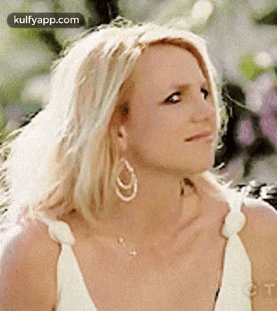 britney spears is wearing a white dress and earrings and looking at the camera .