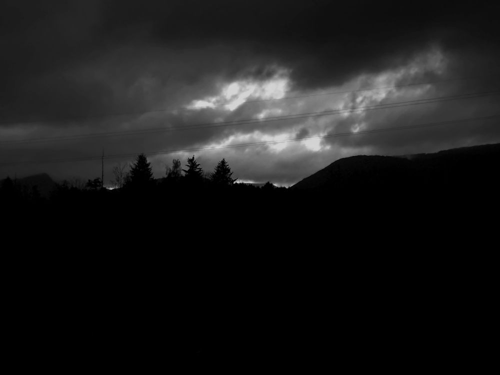 Black and white of photo.
Shows a sillouette of hills and trees while the clouds are hanging dangerously from the sky.