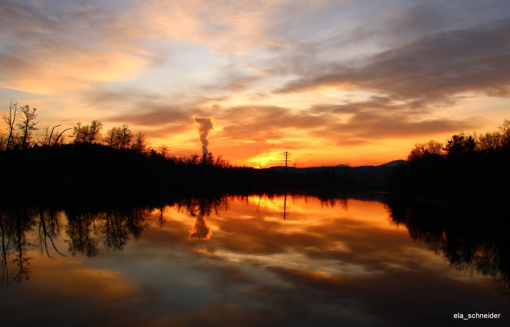 Sunset over river Aare, Switzerland.
Terrific sky with orange, grey and blue colors with clouds reflecting in the river. On the öeft and right side there are the silouettes of trees