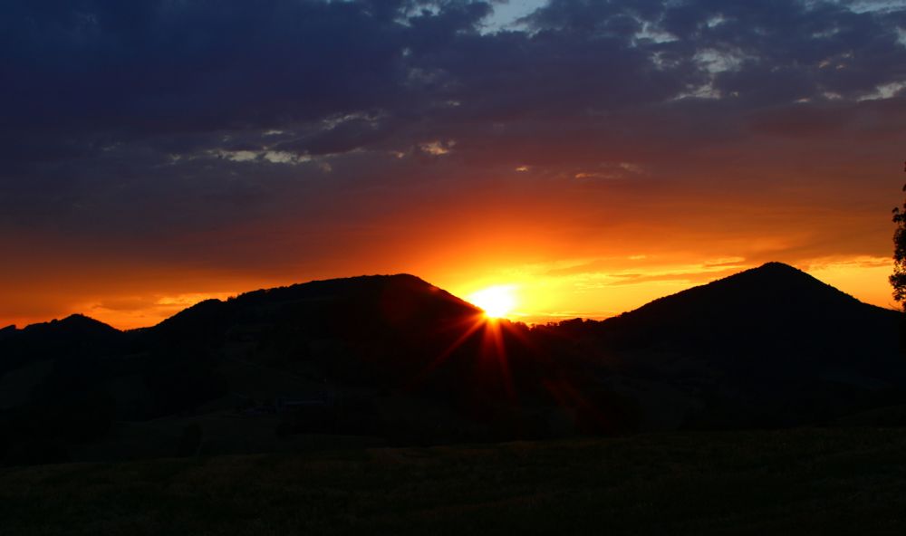Sunset. Silouette of hills before a yellow-orange background and grey-blue clouds above it