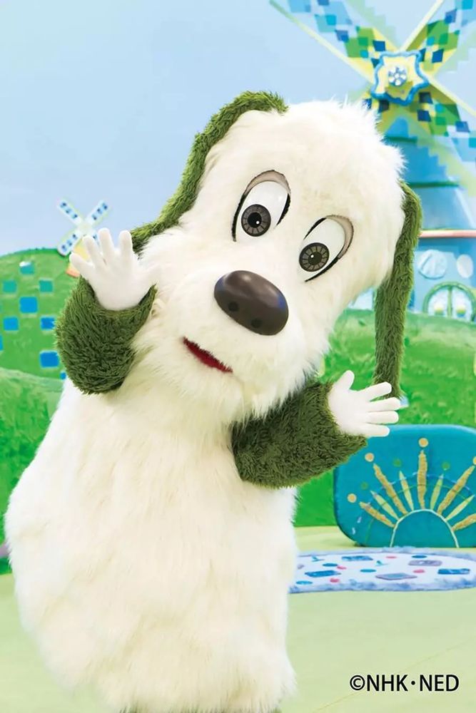 Eテレいないいないばぁっ！に出演中の白いボディで手足がオリーブグリーン色の犬のキャラクター、ワンワンの着ぐるみが両手を顔の横でぱあっと開いている姿