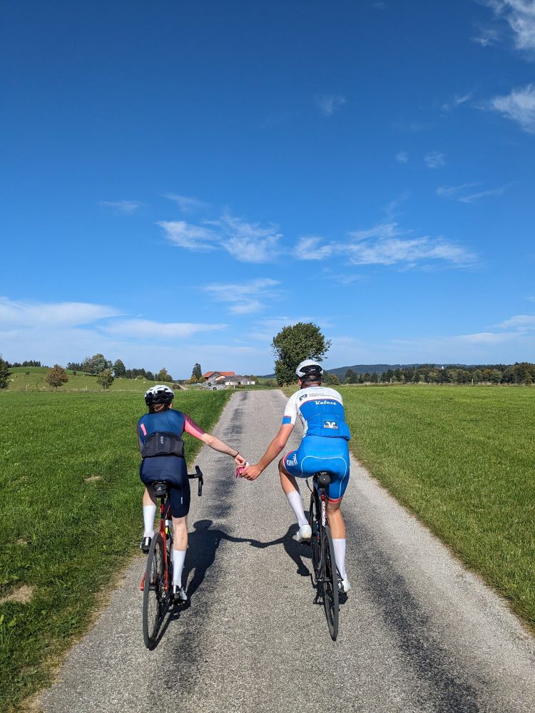 Zwei radportler fahren zwischen den Wiesen. Eine reicht in voller Fahrt eine Packung Süßigkeiten der andere greift rein.