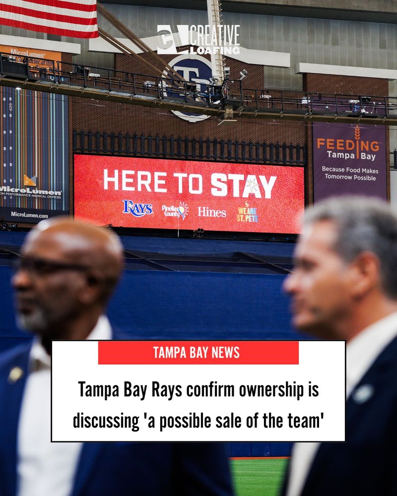 A news graphic with the headline: Tampa Bay Rays confirm ownership is discussing 'a possible sale of the team'
The photo is taken inside Tropicana Field, the Tampa Bay Rays' indoor baseball stadium. On the digital scoreboard is a sign that says "HERE TO STAY" in white letters on a red background. Blurred in the foreground are St. Petersburg's Mayor Ken Welch to the left and the baseball team's owner Stu Sternberg on the right.