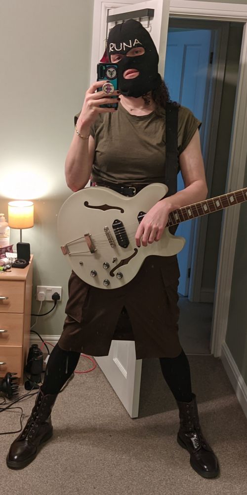 selfie taken by me, runa, a white woman. i'm dressed as james dean bradfield from manic street preachers on top of the pops in 1994 playing 'faster'. i've got an army green top and a black bally with my name stitched on it in white. i'm posing with my white epiphone casino because that's the closest thing i have to a les paul. also my legs don't go as far apart as jdb's because of my skirt. 